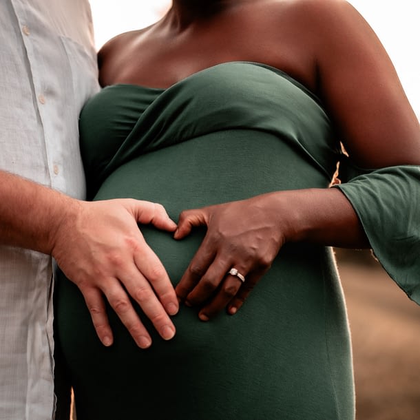 A mother and father to be forming a heart on her belly.