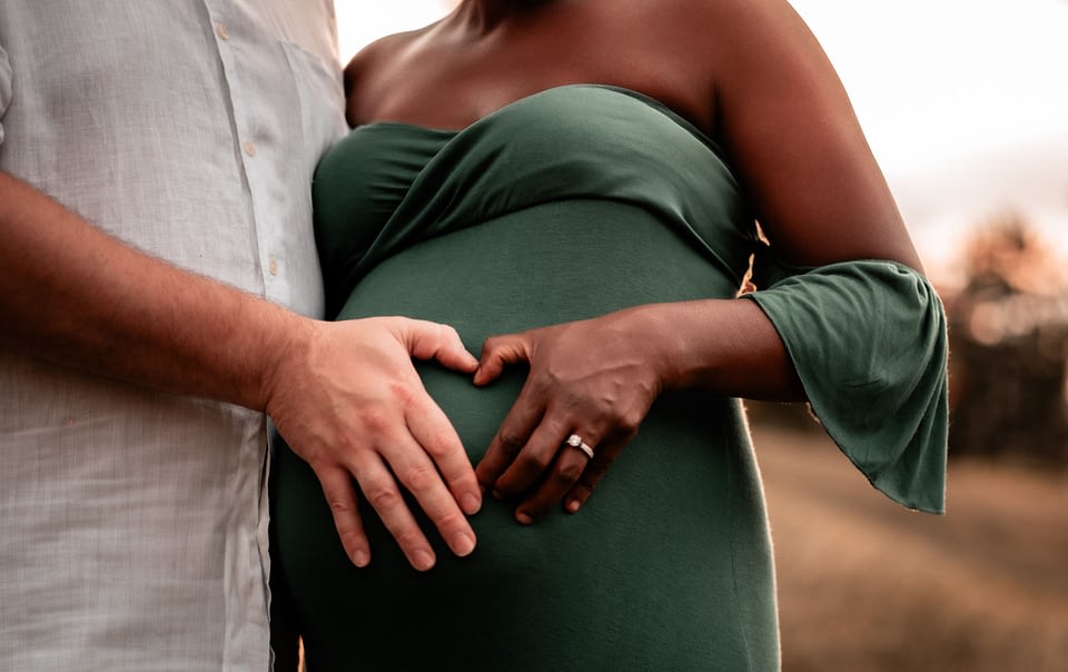 A mother and father to be forming a heart on her belly.