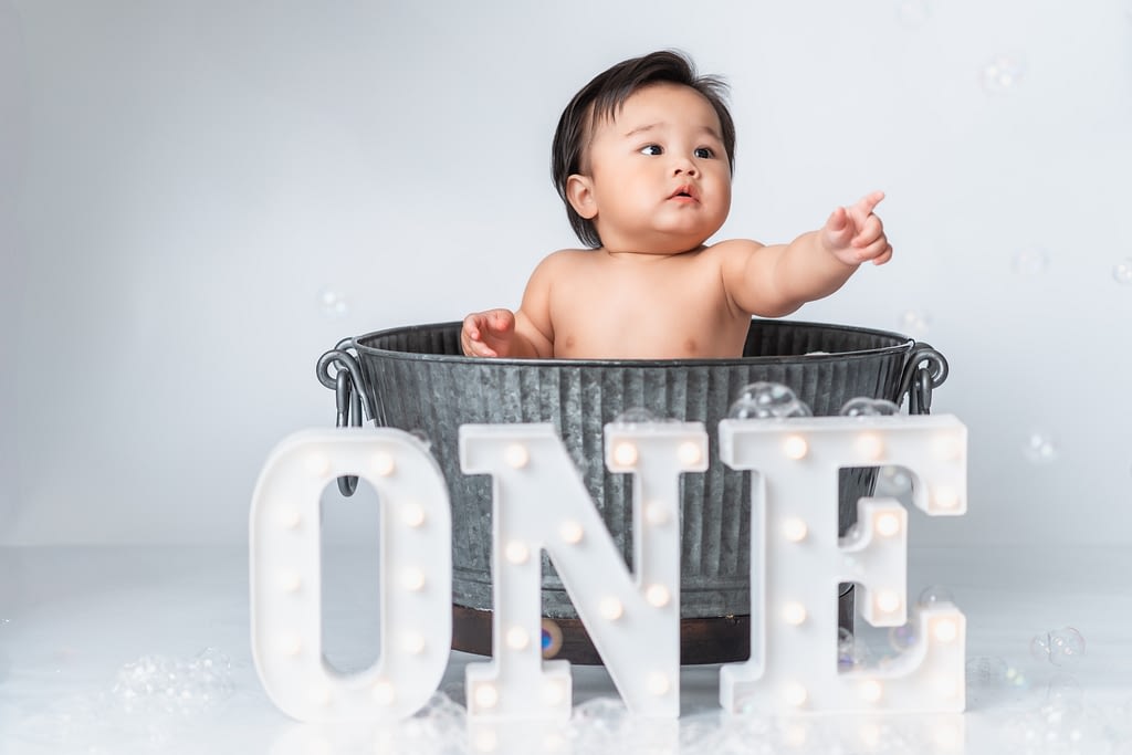 A baby boy pointing from a metal bath tub for his first birthday portraits.