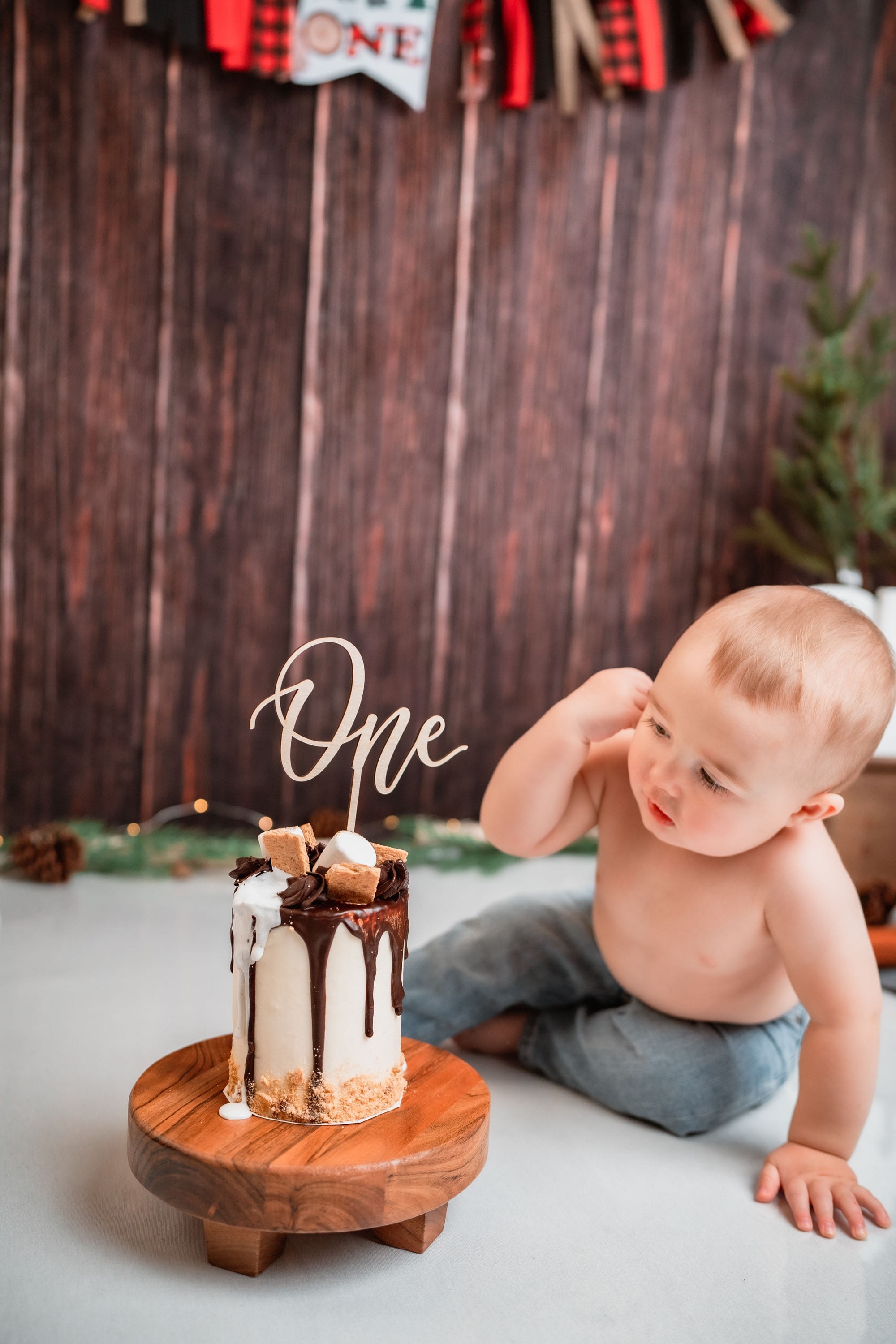 A one year old baby boy celebrating his birthday with a smores cake cake smash in a home studio.