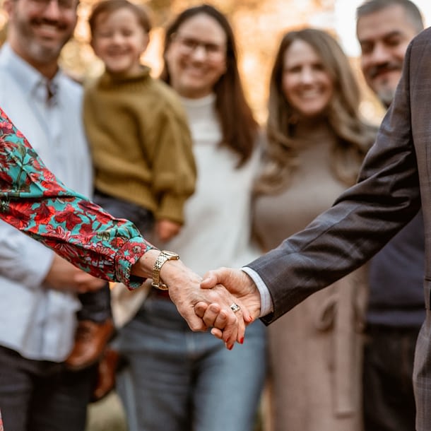 Close-up of an elderly couple holding hands during a family photo session at Carlyle House, with their smiling family softly blurred in the background.