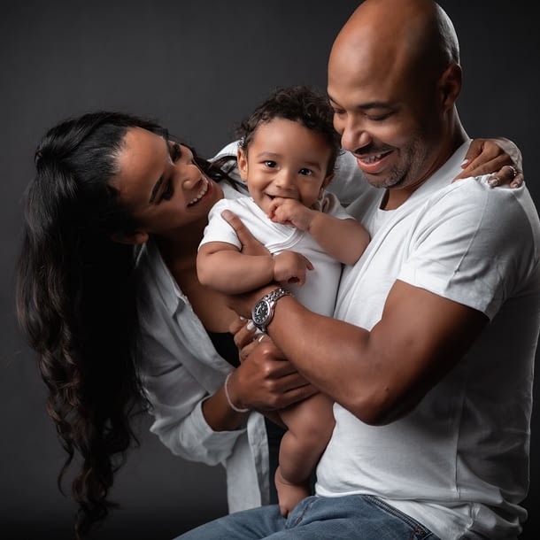 A family of three photographed against a black studio backdrop.