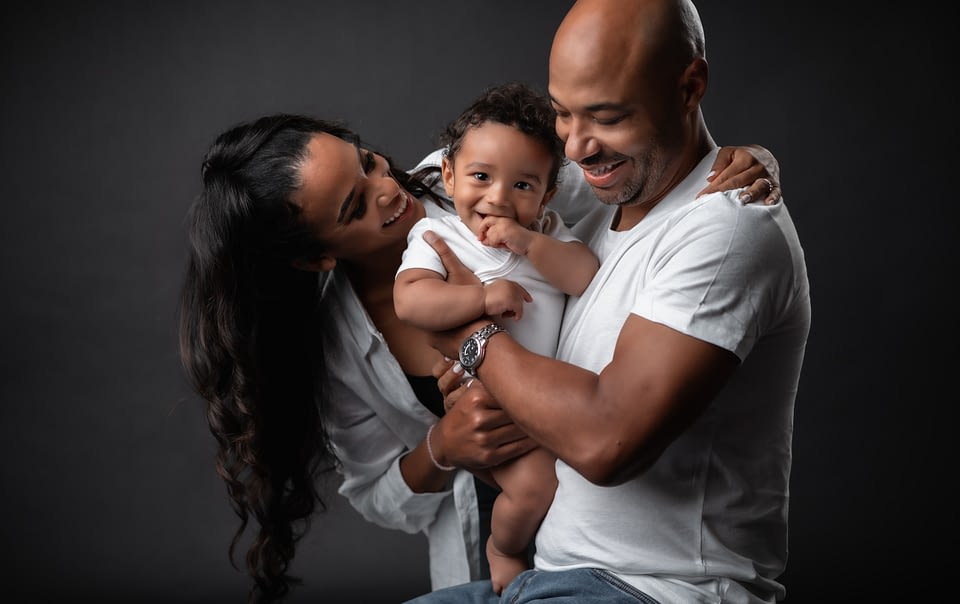 A family of three photographed against a black studio backdrop.