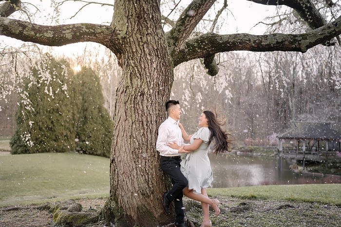 Engaged couple laughing under cherry blossoms at sunrise during spring engagement session at Brookside Gardens